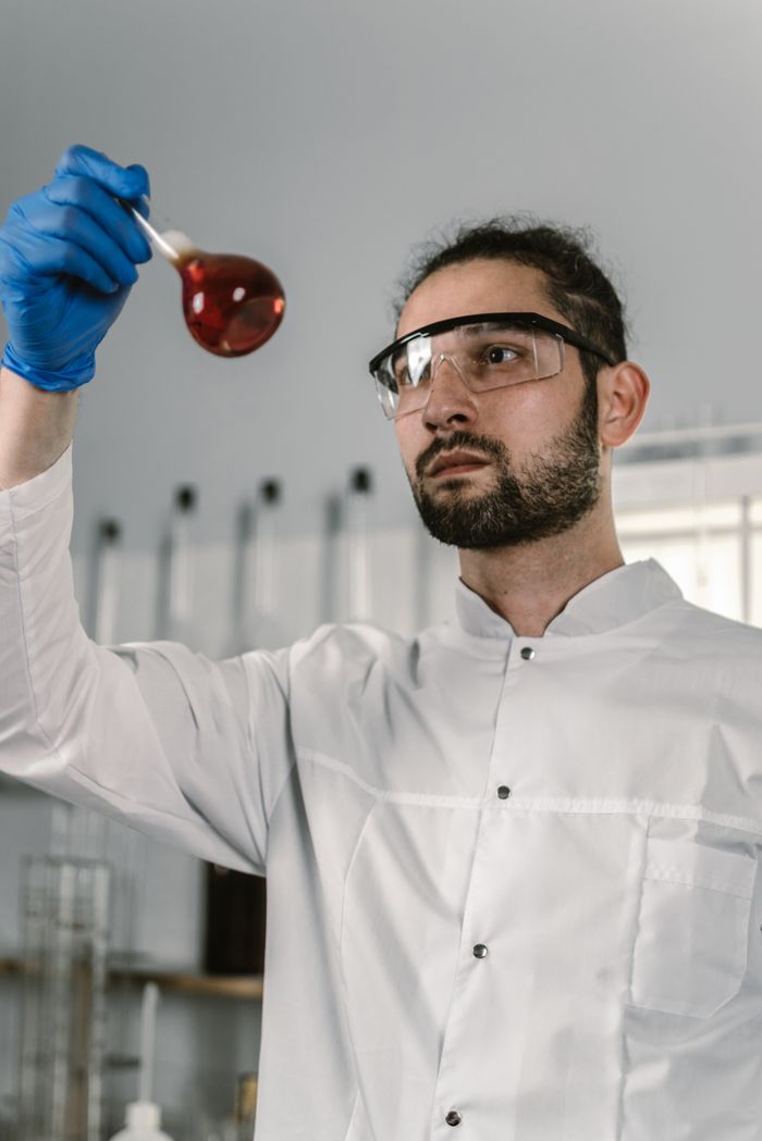 A scientist wearing protective gear analyzing a liquid sample in a laboratory setting.